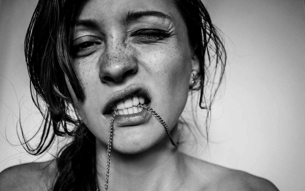 black and white of girl with freckles chewing her necklace